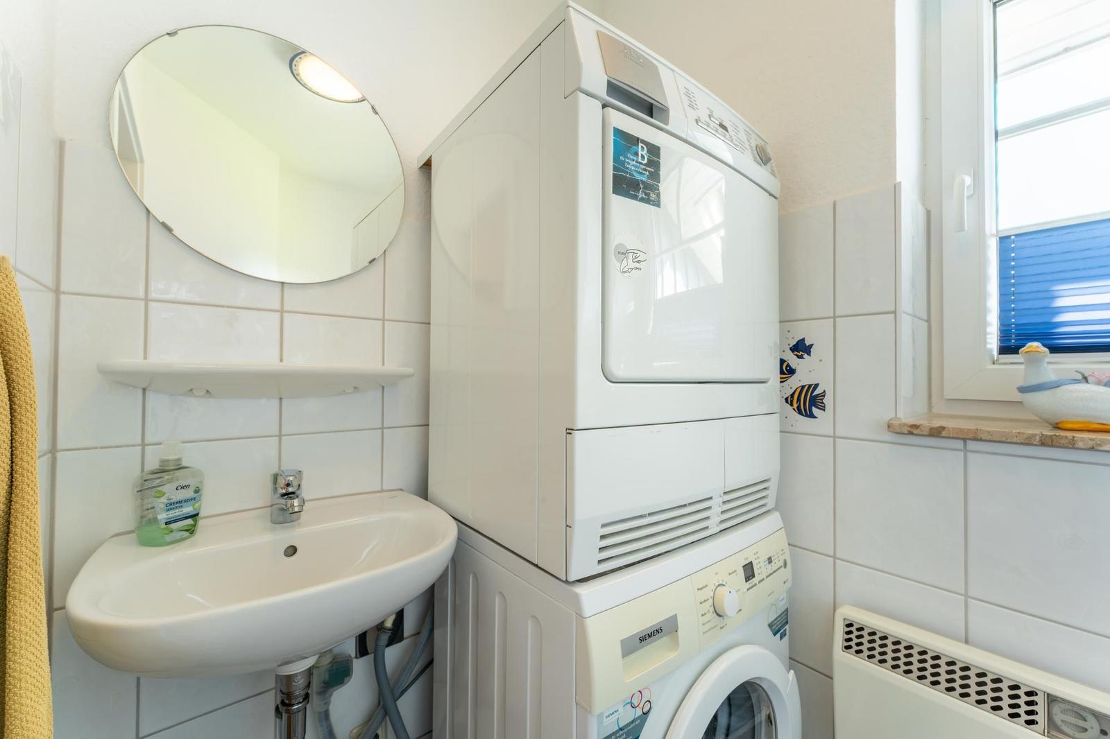 Waschmaschine und Trockner stehen in einem Raum mit Waschbecken und Spiegel.