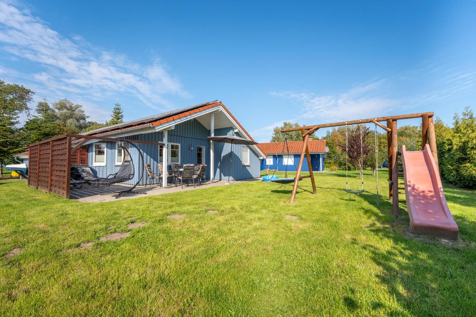 Blau gestrichenes Ferienhaus mit Spielplatz und Terrasse im Garten.