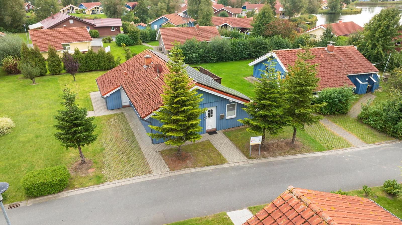 Blau gestrichenes Haus mit rotem Dach und grünem Garten. Neben ihm ein weiteres Haus.