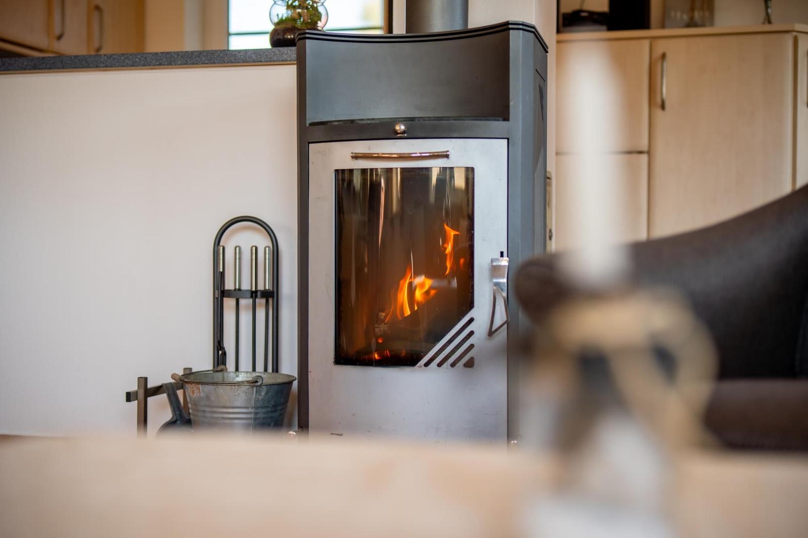 Ein Kaminofen mit brennendem Holz steht im Wohnbereich. Im Hintergrund sind Küchenschränke zu sehen.