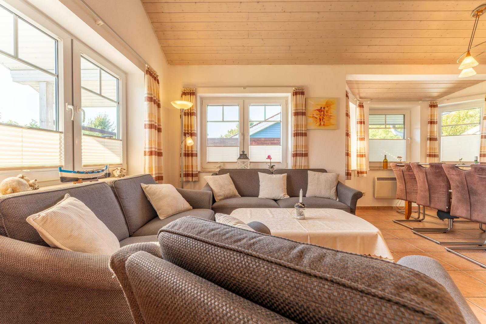 Wohn- und Essbereich mit Sofa, Tisch und Fenstern.