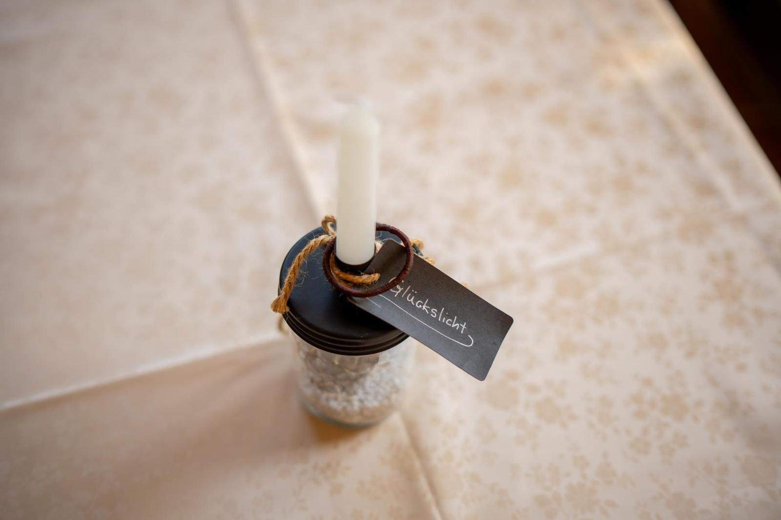 Eine Kerze in einem Glasbehälter mit Etikett und Schnur auf Tischdecke.