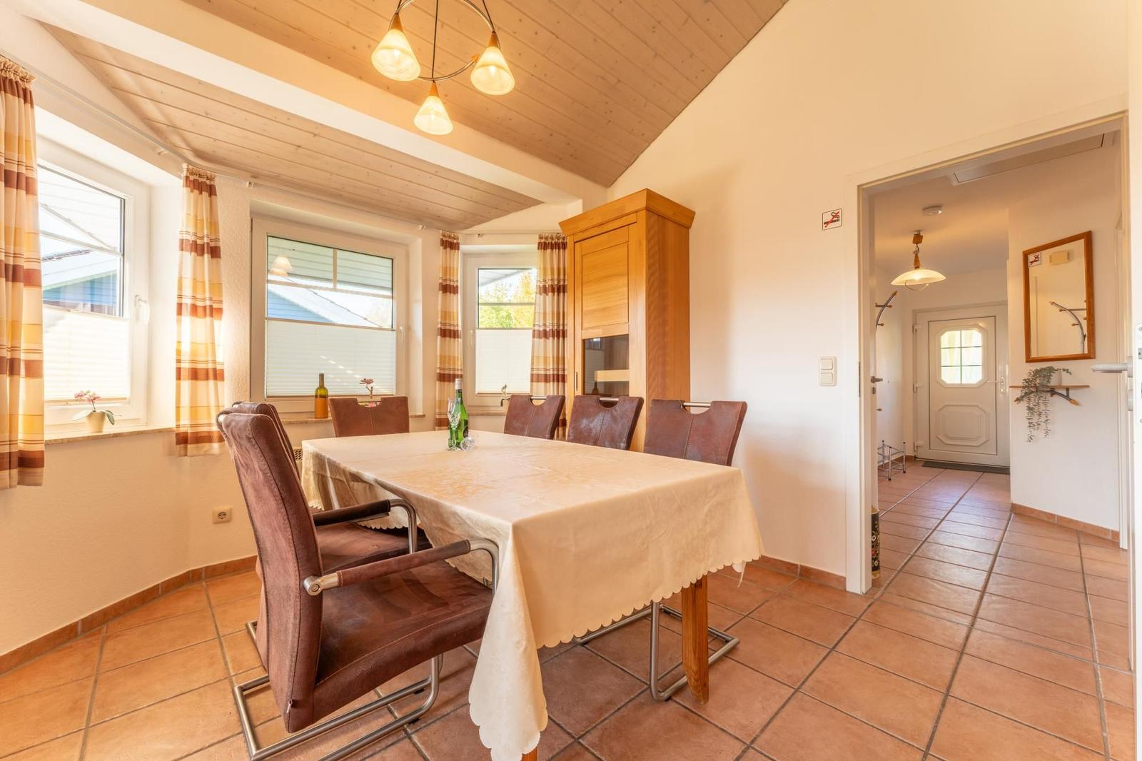Esszimmer mit Holzdecke, Tisch mit Tischdecke und Stühlen, Fenster mit Vorhängen.