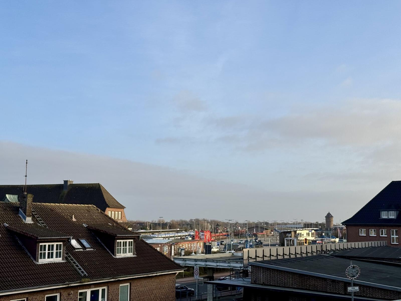 Stadtblick mit Dächern, Straßen und einem Wasserturm unter blauem Himmel.