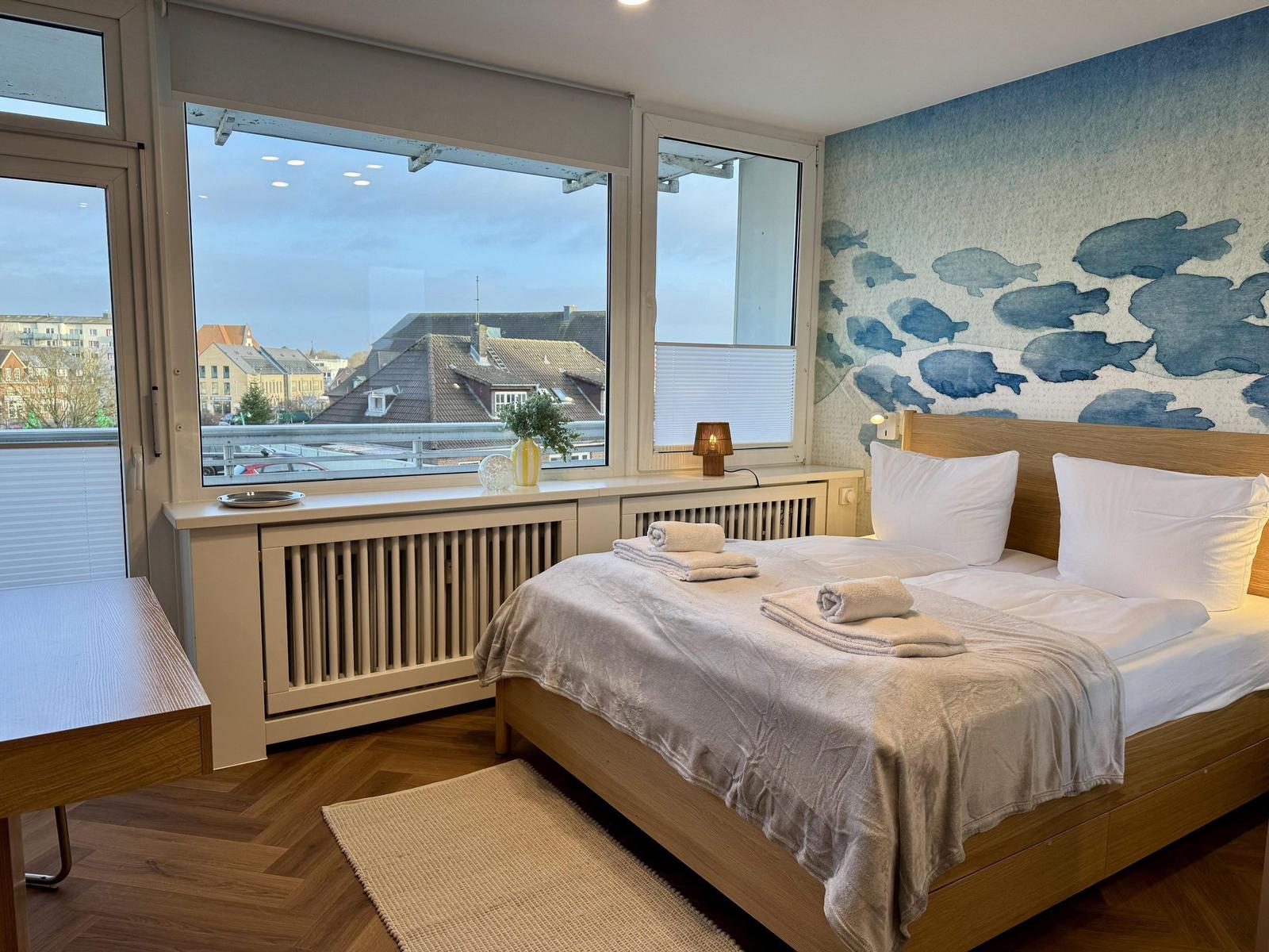 Schlafzimmer mit Bett, Fensterblick und Fischwand.