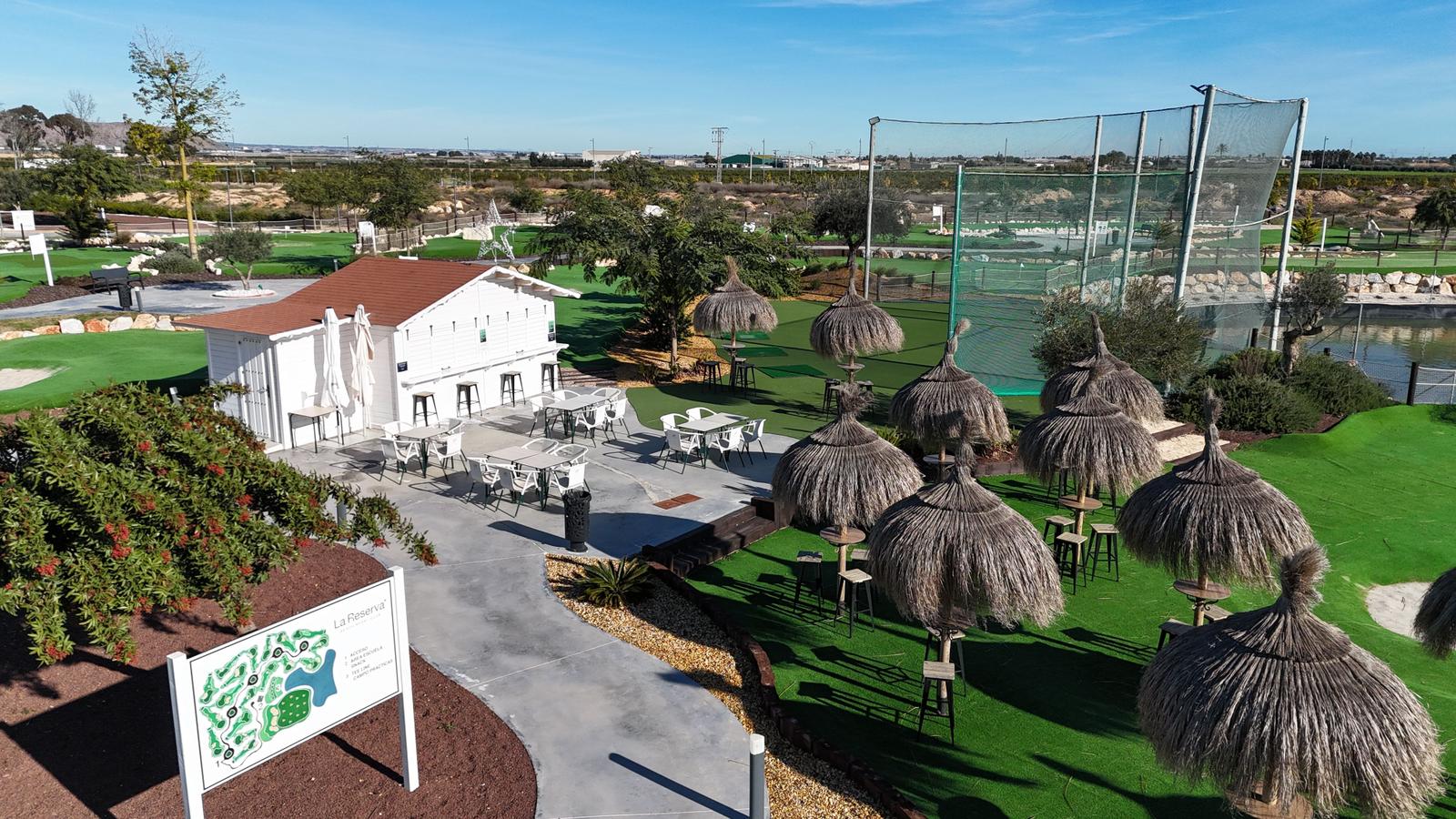 Golf course with lounge area and practice range with thatched umbrellas.