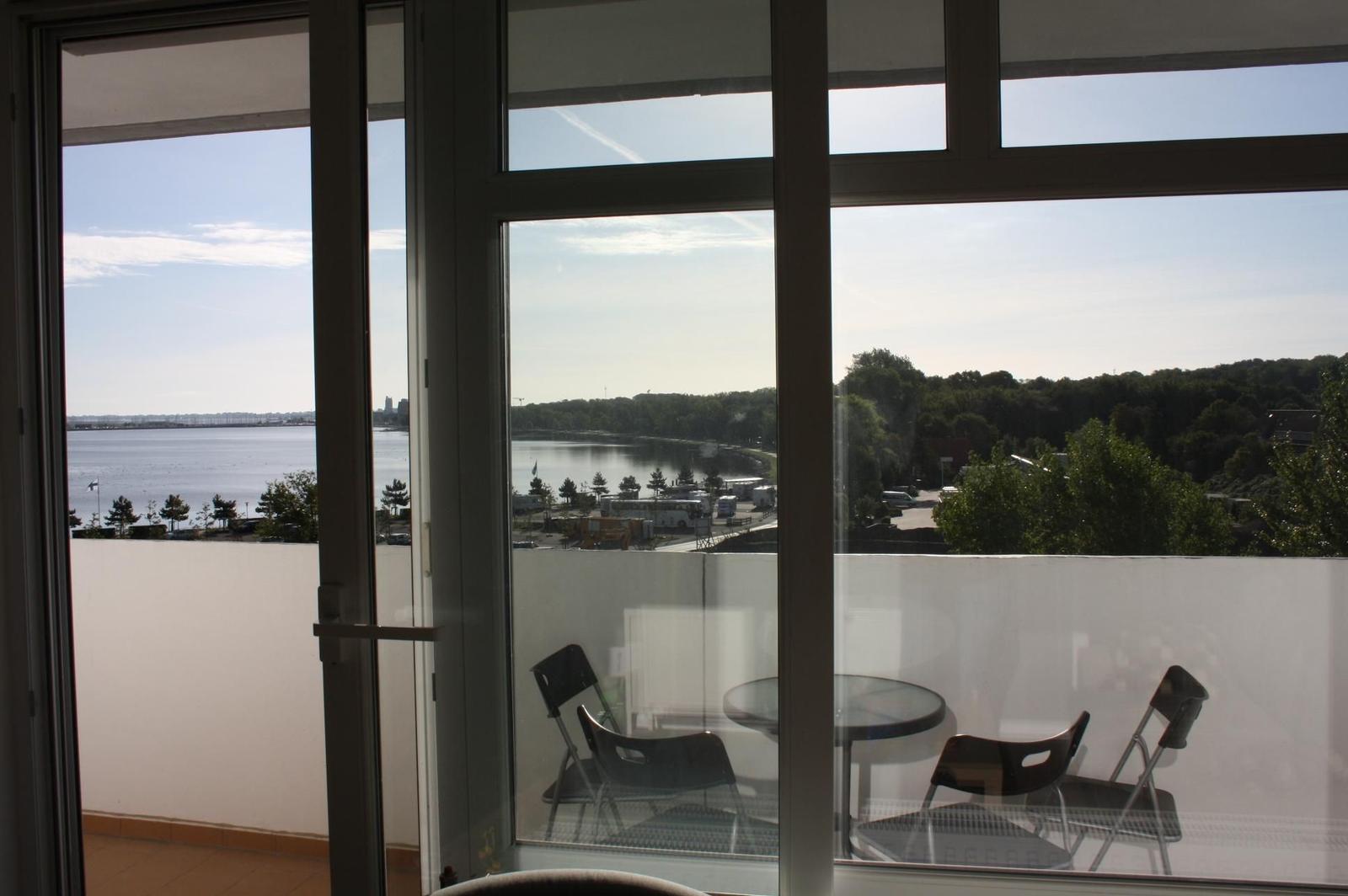 Blick auf Wasser und Grün von der Terrasse mit Tisch und Stühlen.