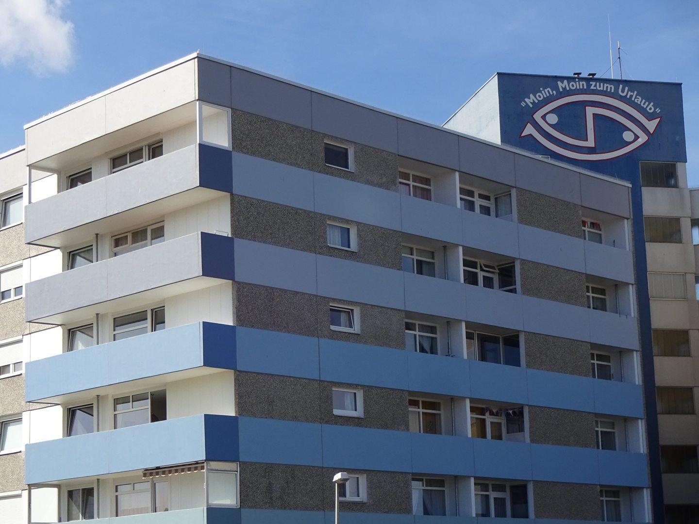 Fünfgeschossiges Wohngebäude mit Balkonen und blau-weißem Fassadendesign.