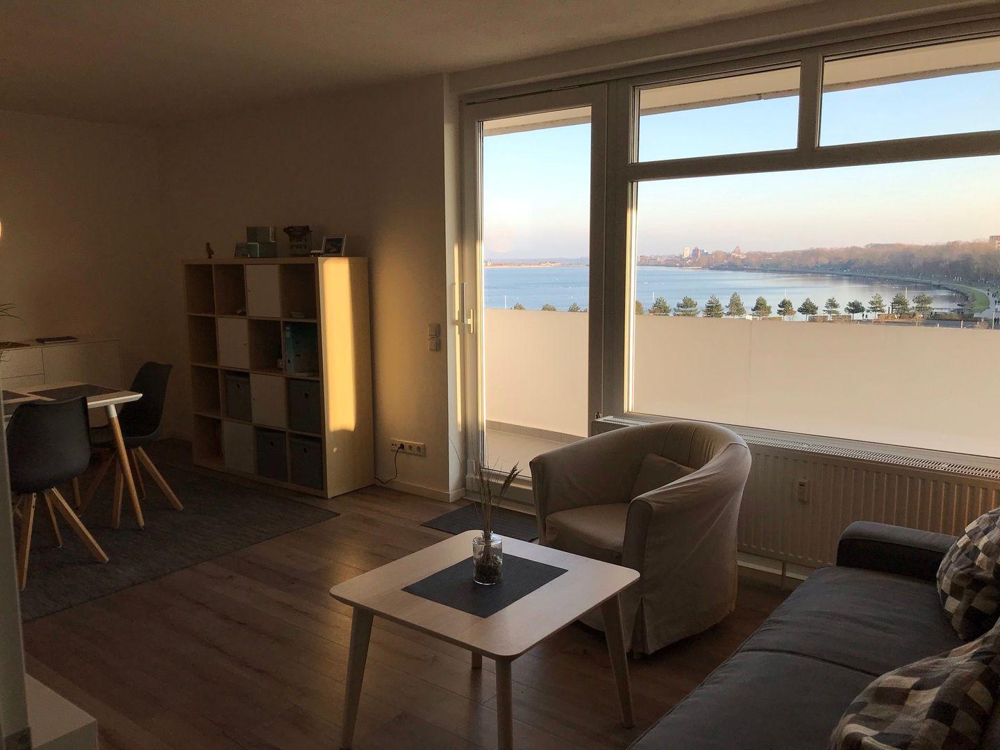 Wohnung mit Blick auf Wasser und Stadt. Sitzgelegenheiten, Tisch, Schrank und Terrasse.