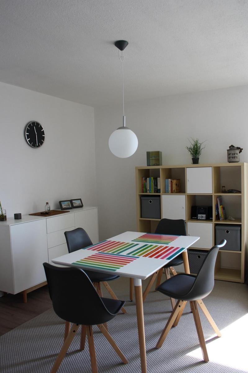 Esszimmer mit Tisch, Stühlen und Regal. Deckenleuchte und Wanduhr sind sichtbar.