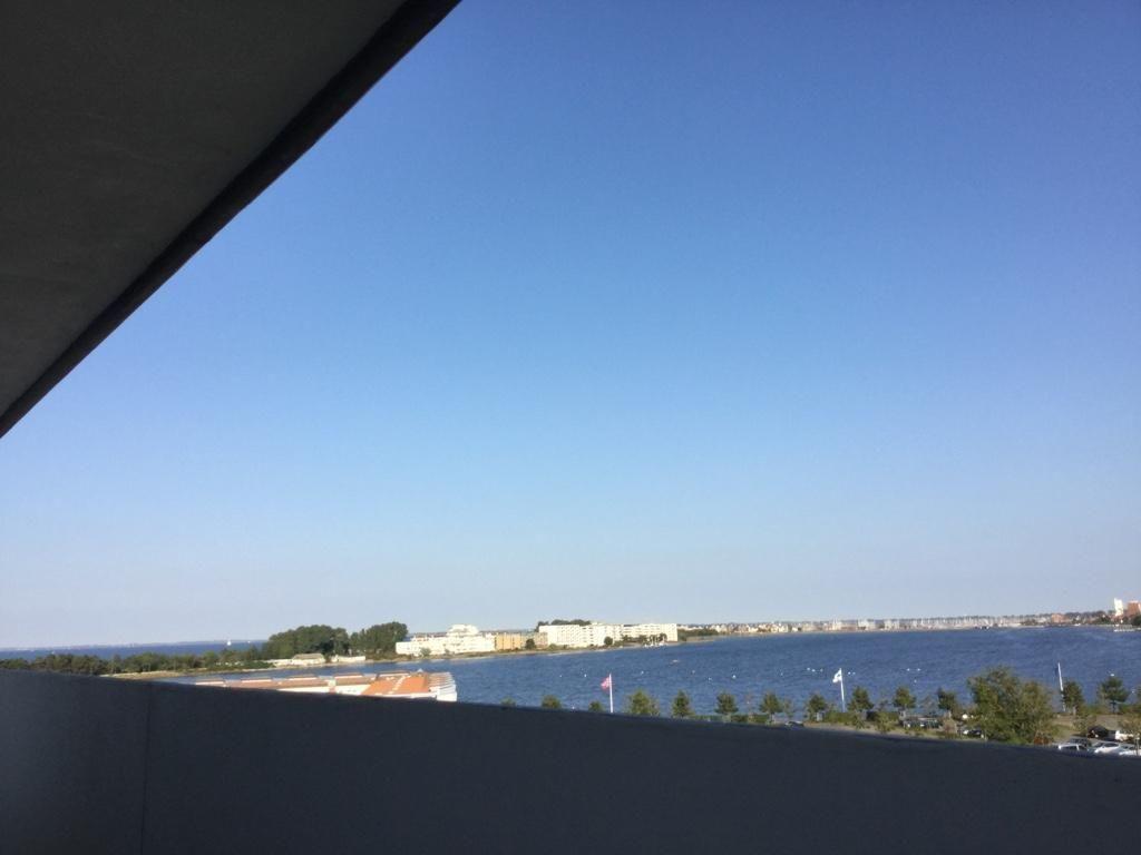 Blick vom Balkon auf einen See mit Uferbebauung und klarem Himmel.