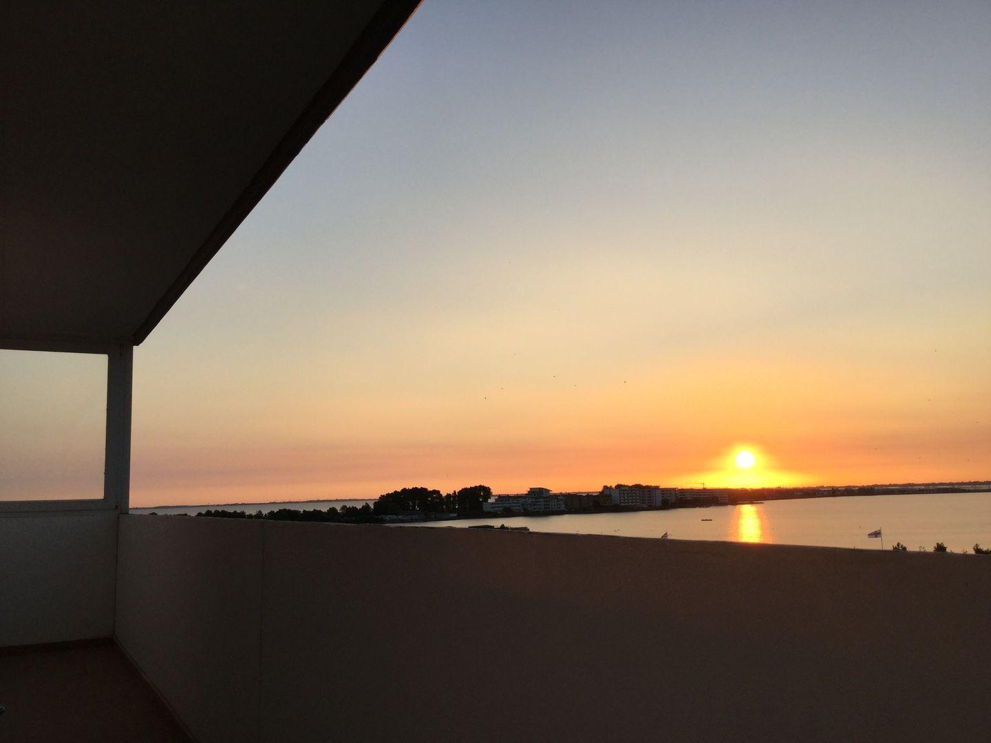 Sonnenuntergang über dem Wasser mit Blick auf Gebäude und Bäume von der Terrasse aus.