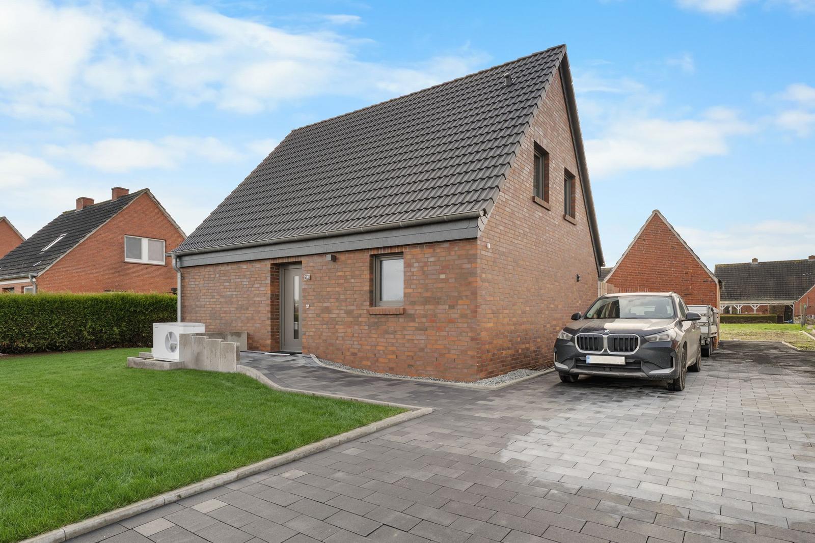 Modernes Haus mit Steinmauer, Garage und gepflasterter Auffahrt. Grünflächen und klare Sicht.
