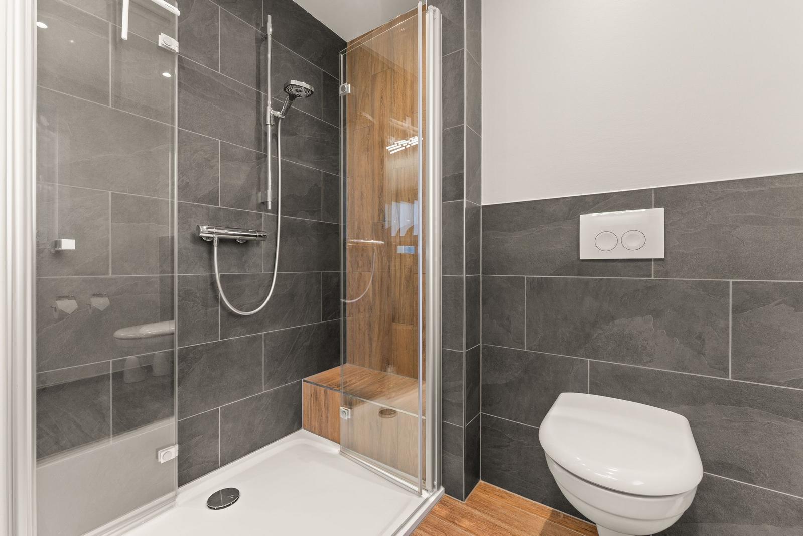 Dusche mit Glaswand, Toilette und Holzbank in moderner Badezimmerausstattung.