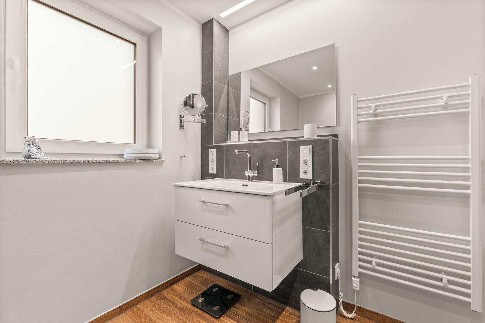 Badezimmer mit Waschbecken, Spiegel, Heizung und Fenster.