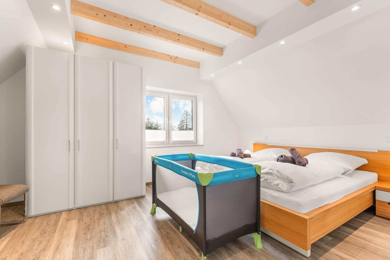 Schlafzimmer mit Doppelbett, Kinderbett und Kleiderschrank unter Dachschrägen.