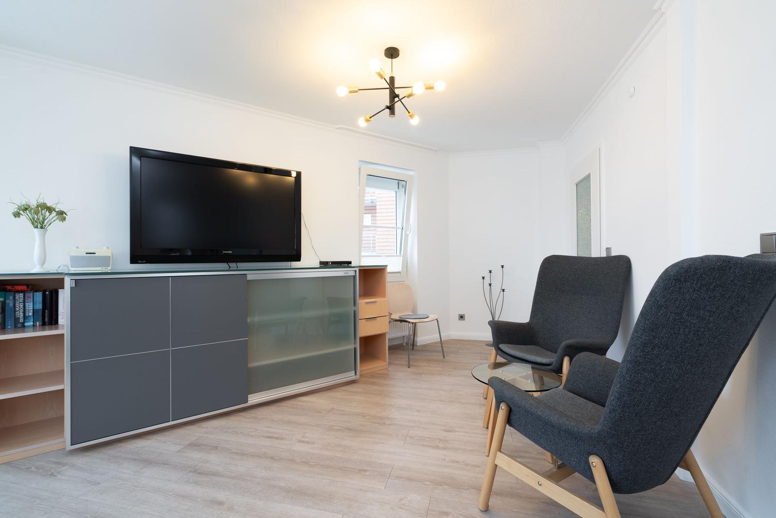 Wohnzimmer mit Fernseher, zwei Sesseln und Holzboden.