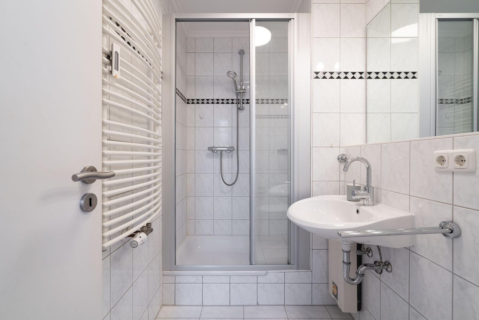 Badezimmer mit Dusche, Waschbecken und Heizkörper
