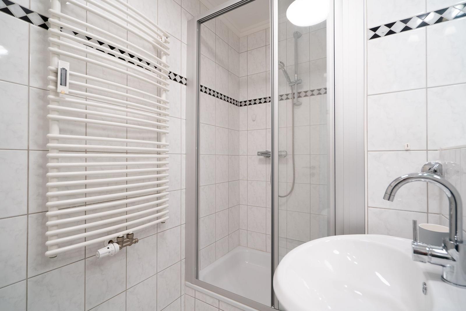 Badezimmer mit Dusche, Waschbecken und Heizkörper