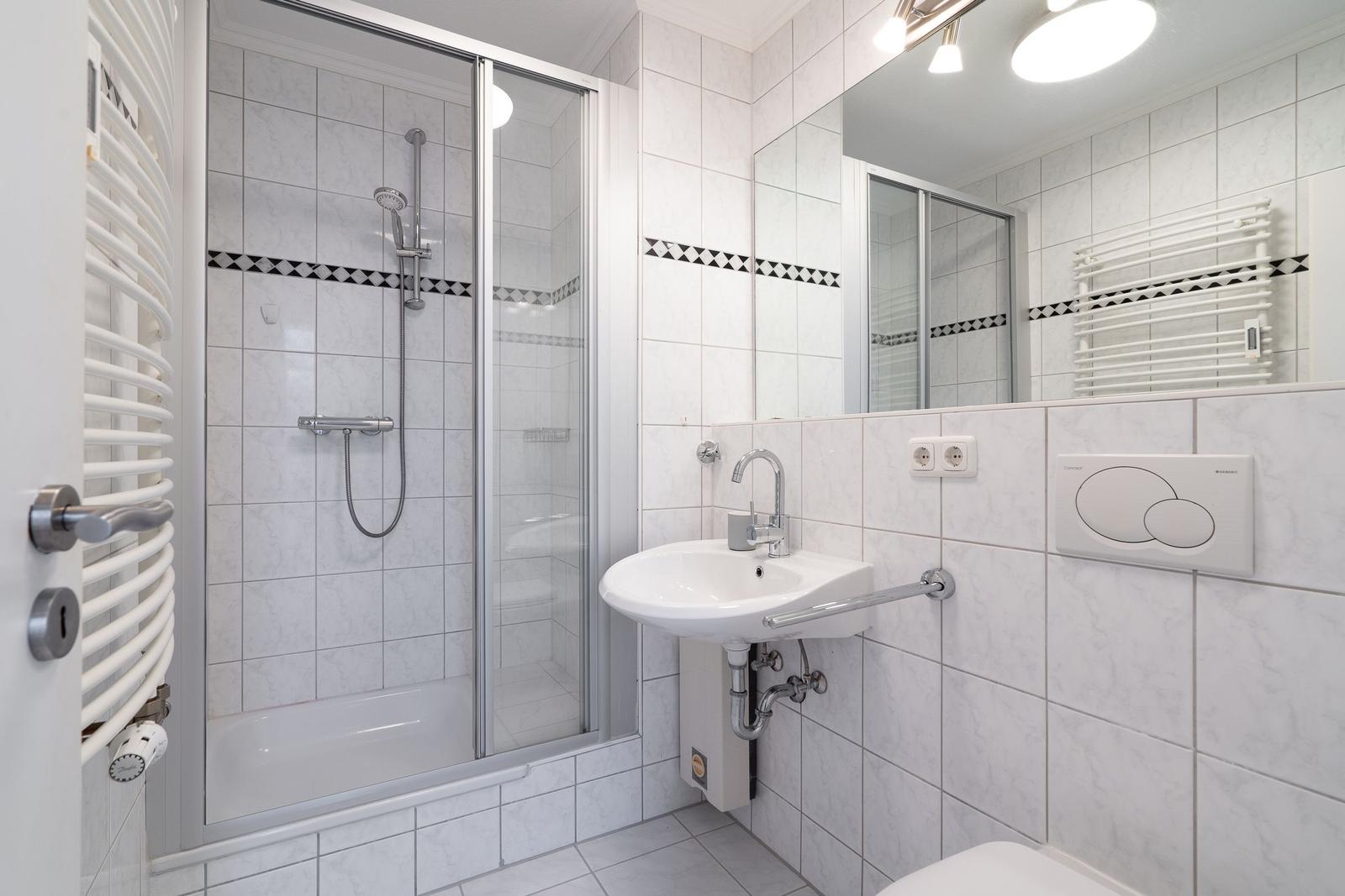 Badezimmer mit Dusche, Waschbecken und Heizkörper