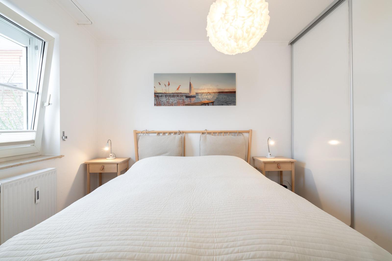 Schlafzimmer mit Bett, Nachttischen und Wandbild. Fenster und Schrank sind sichtbar.