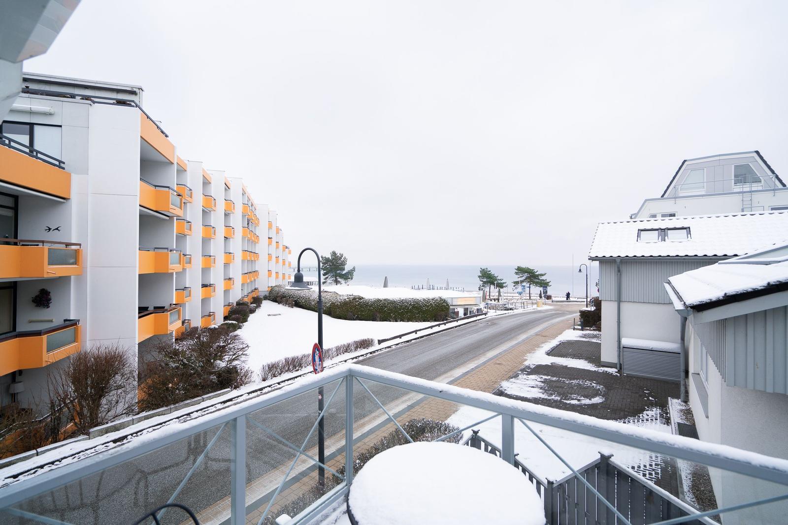Blick vom Balkon auf schneebedeckte Straße, Strand und Gebäude.