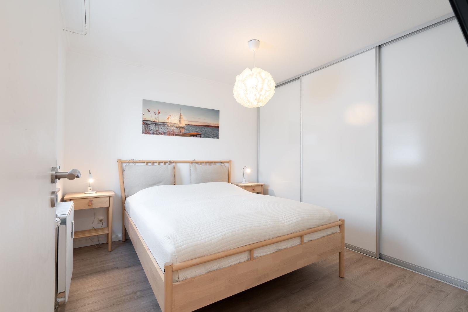 Schlafzimmer mit Bett, Nachttischen und Schiebetüren. Wandbild und Deckenleuchte.