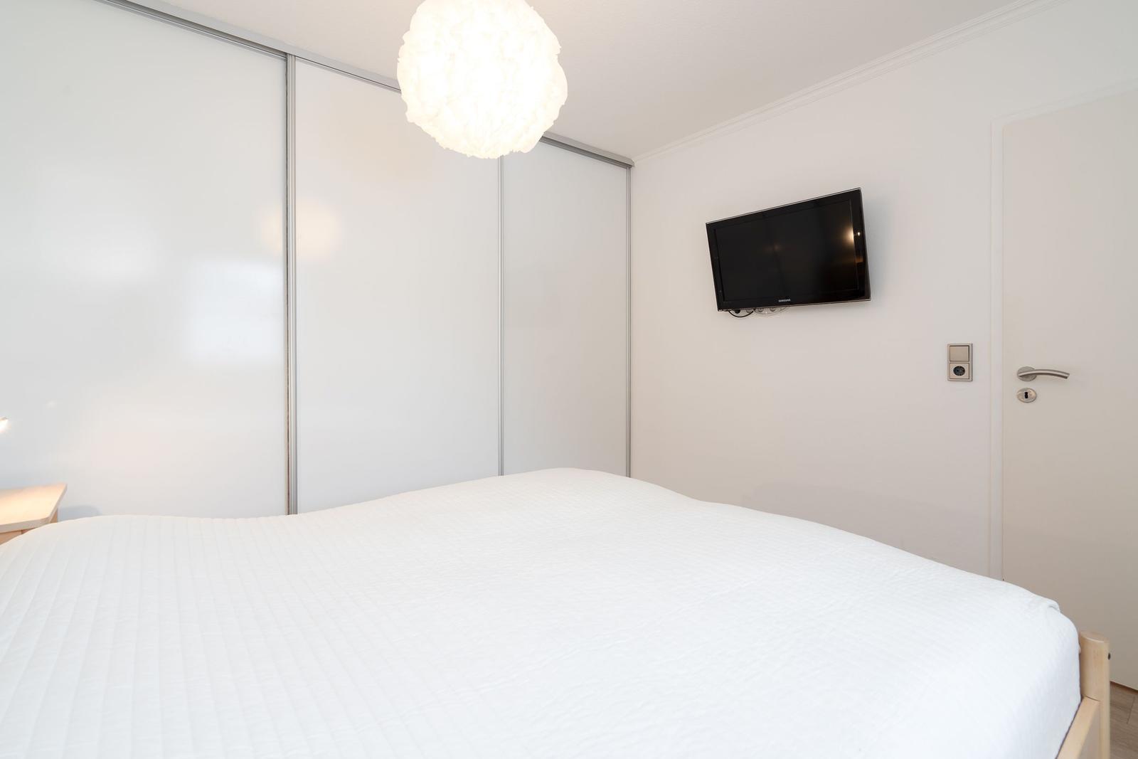 Schlafzimmer mit Bett, Schwebetüren und Wandfernseher.
