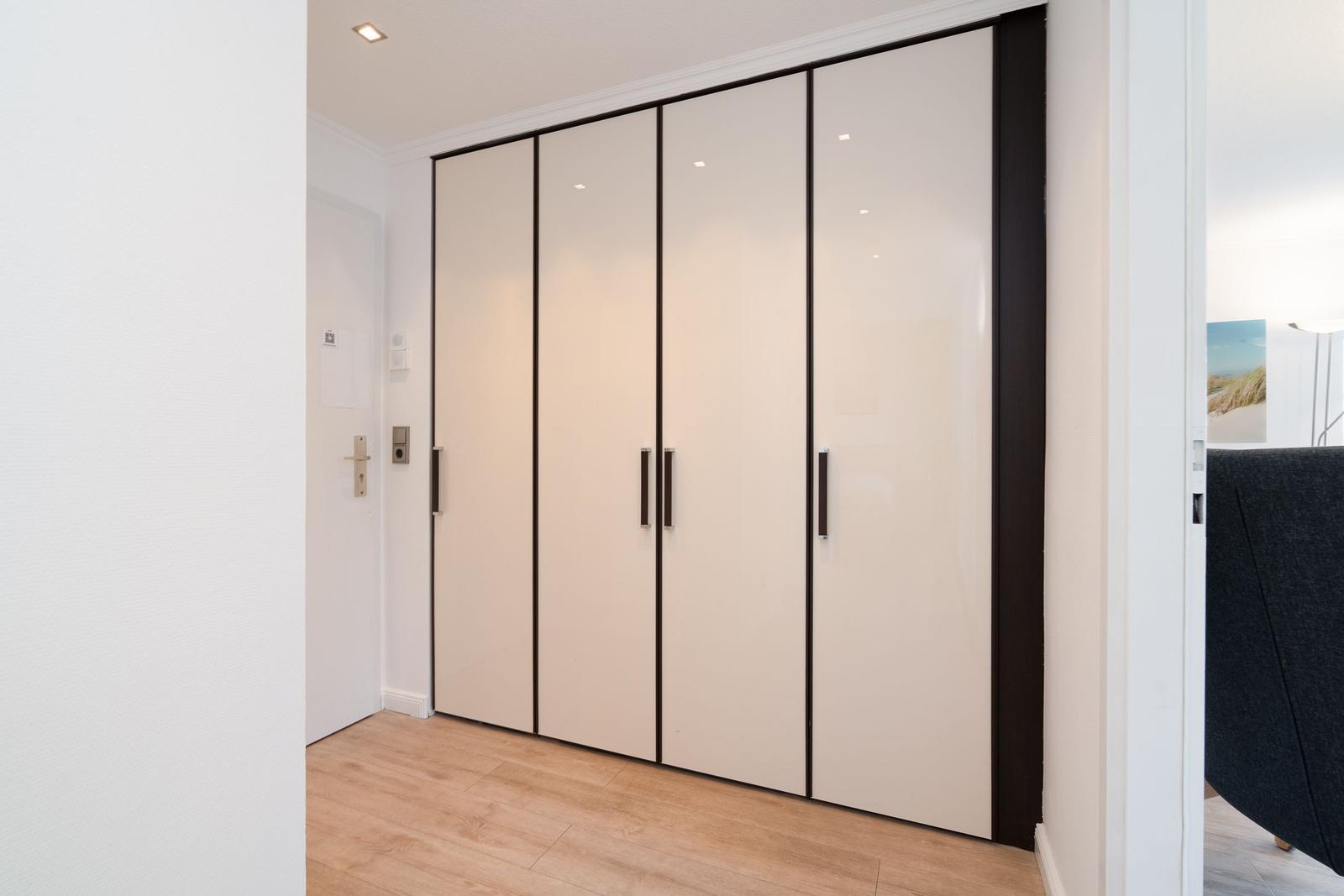 Schwebetüren-Schrank mit dunklen Rahmen und Griffen. Holzfußboden und weiße Wände.