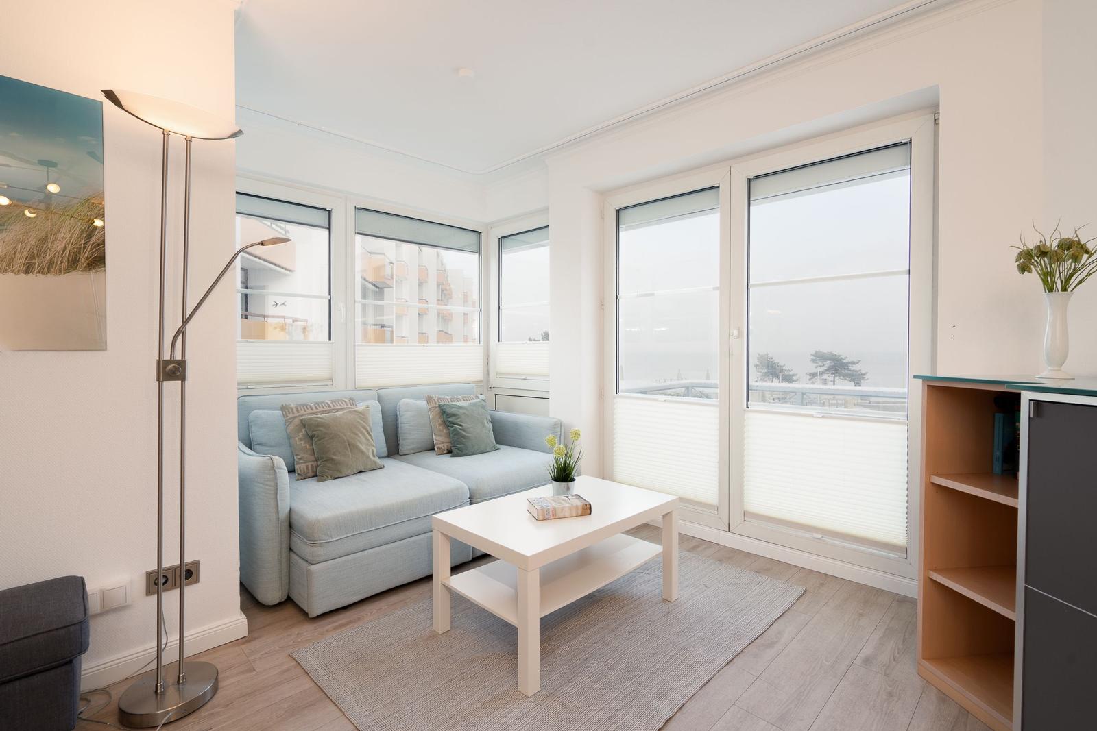 Wohnzimmer mit Sofa, Tisch und großen Fenstern mit Meerblick.