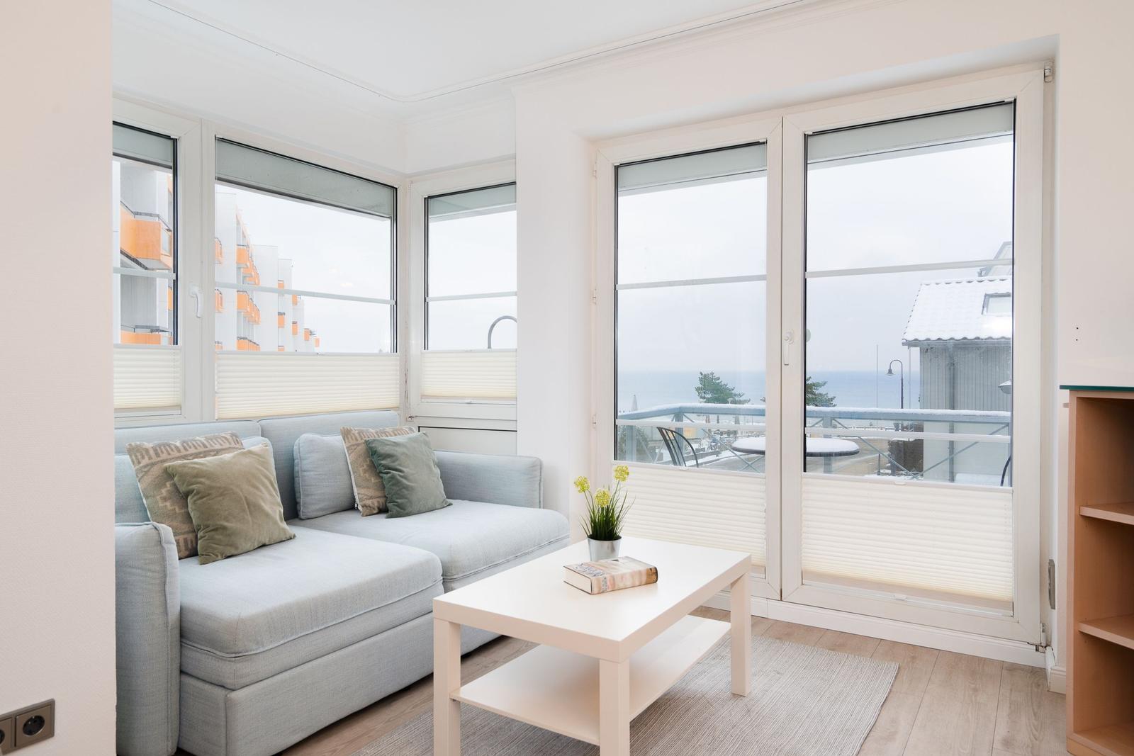 Wohnzimmer mit Sofa, Tisch und großen Fenstern zum Meer