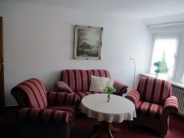 Wohnzimmer mit gestreiftem Sofa und zwei Sesseln um runden Tisch.