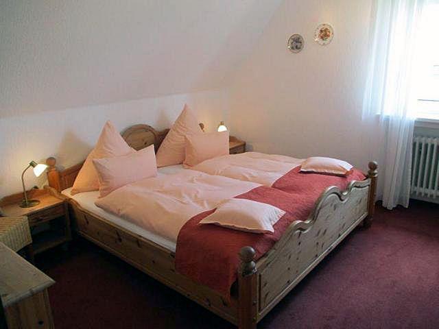 Doppelbett mit Holzrahmen, Nachttische und Fenster mit Vorhängen.