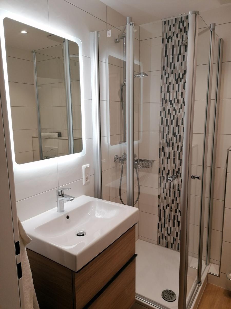 Badezimmer mit Dusche, Waschbecken und beleuchtetem Spiegel.