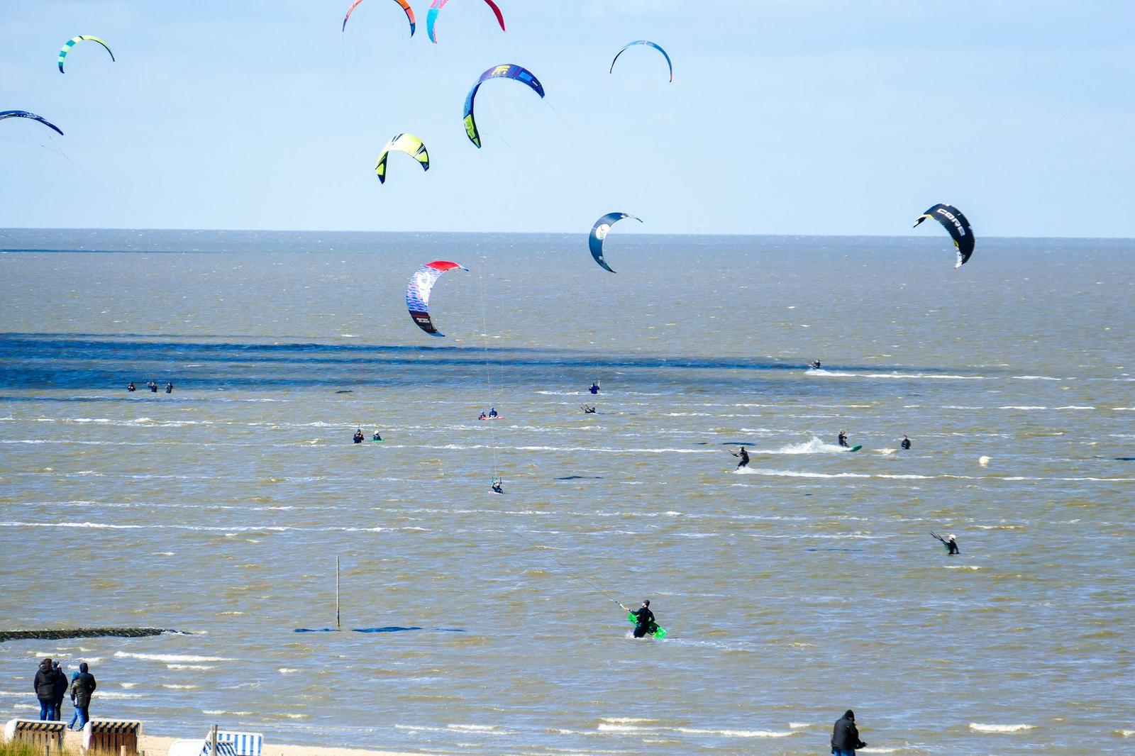 Mehrere Kitesurfer üben auf dem Meer. Einige Personen stehen am Strand.