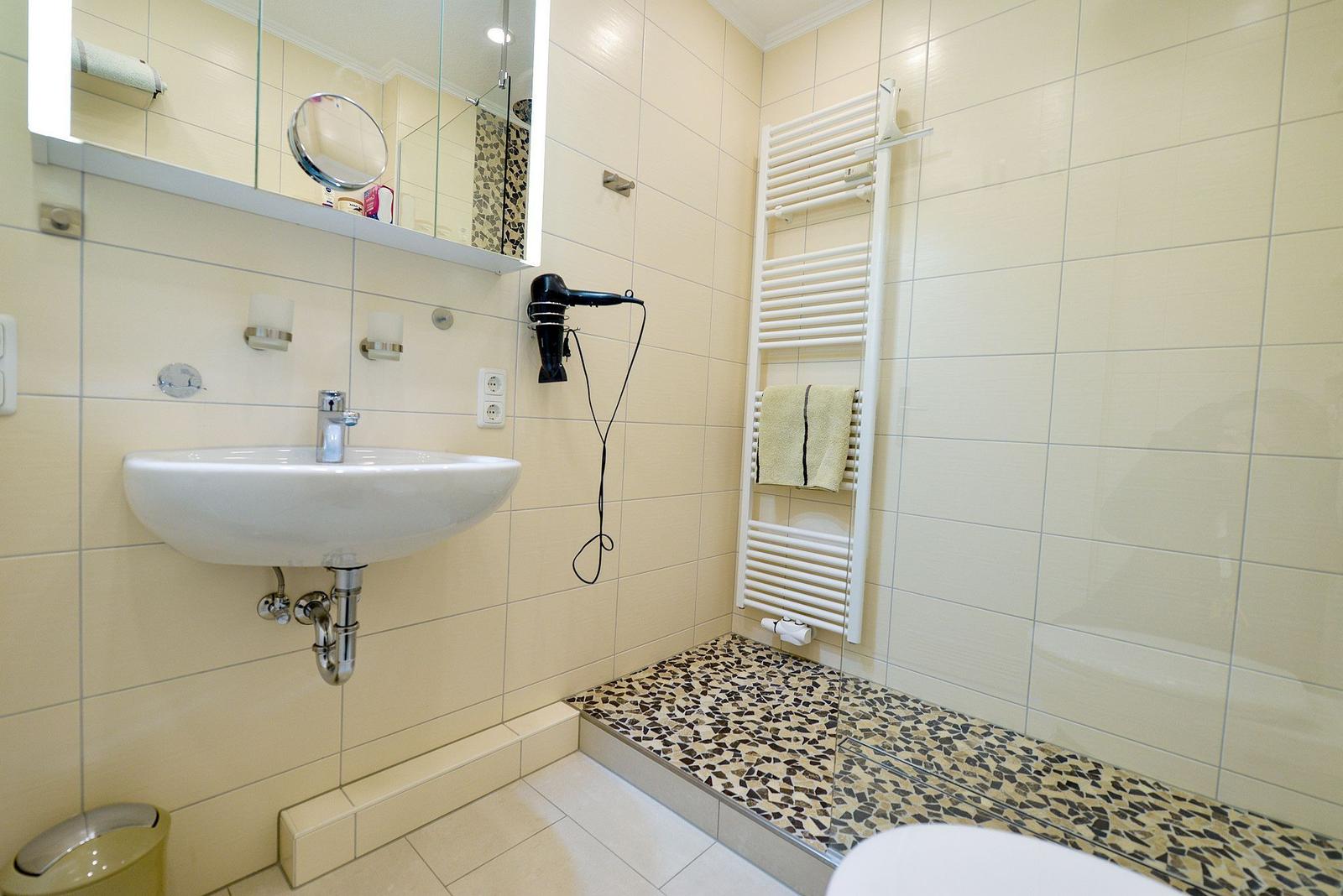 Badezimmer mit Waschbecken, Spiegel, Haartrockner und Dusche mit Mosaikboden.