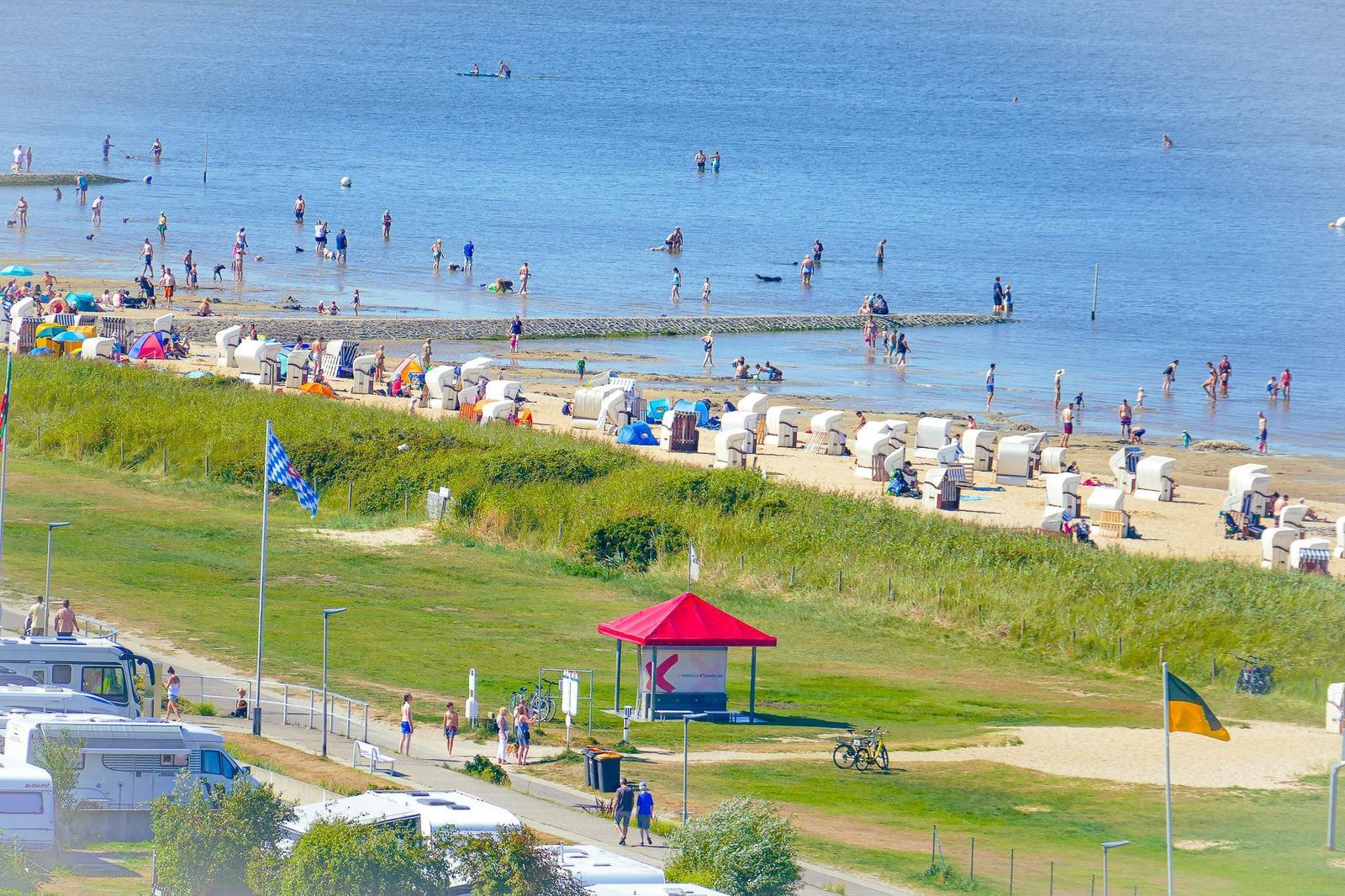 Strand mit Badegästen, Strandkörben und grünen Dünen im Hintergrund.