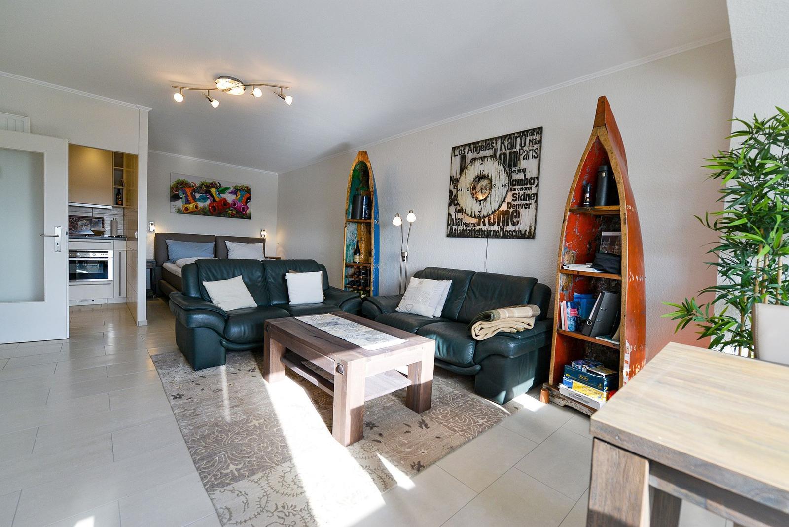 Wohnzimmer mit zwei Sofas, Tisch und Wanddekoration. Küche im Hintergrund sichtbar.