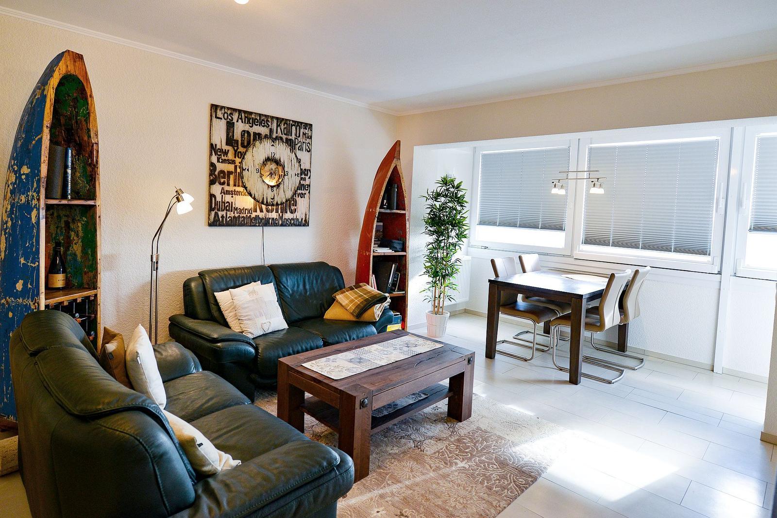 Wohn- und Essbereich mit Sofa, Tisch und Fenstern.