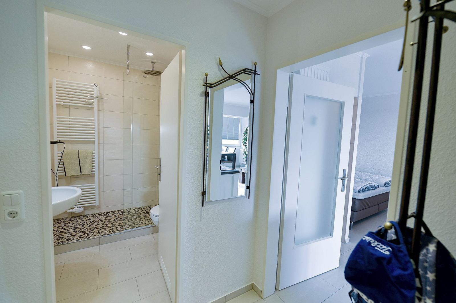 Flur mit Bad und Schlafzimmer. Spiegel, Badewanne, Dusche und Bett sichtbar.
