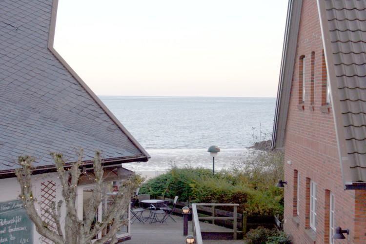 Meerblick zwischen zwei Gebäuden mit Terrasse und Gartenbereich.