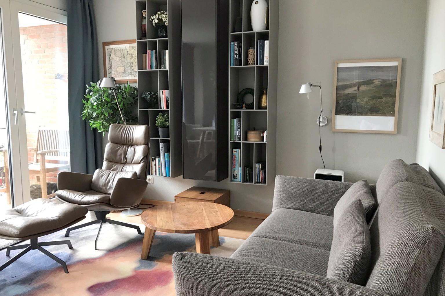 Wohnzimmer mit Sofa, Sessel, Couchtisch und Bücherregal. Durchgang zur Terrasse.