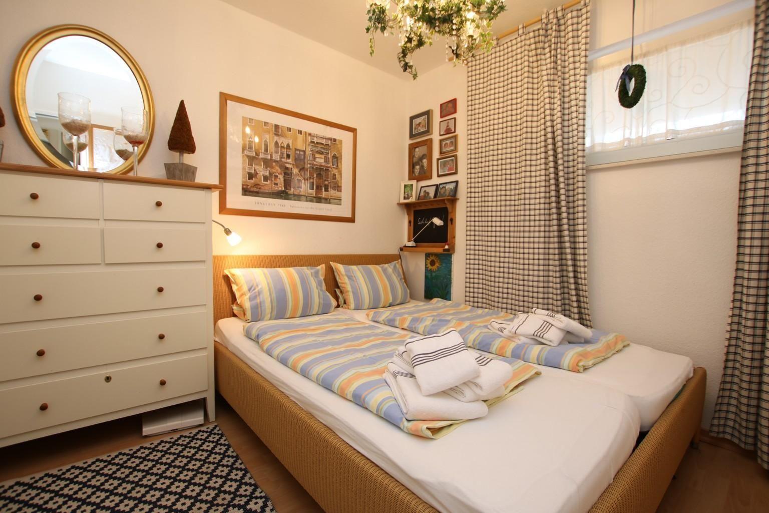 Schlafzimmer mit Doppelbett, Schrank, Wandbild und Vorhängen.