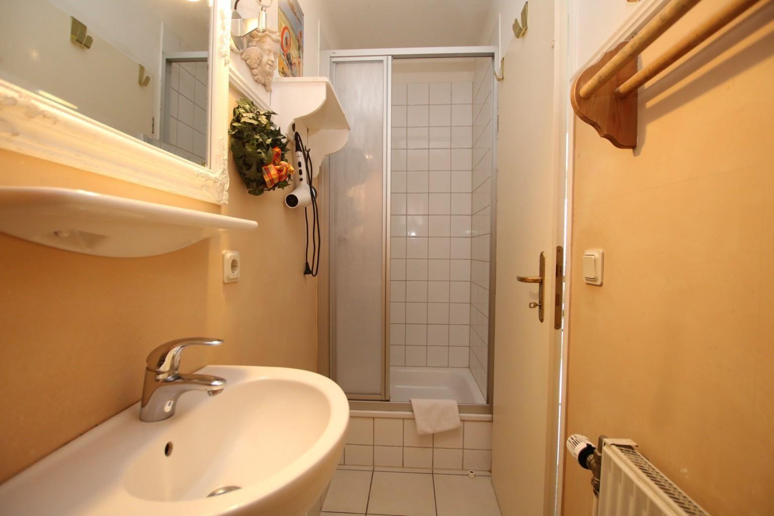 Bad mit Waschbecken, Spiegel, Dusche und Handtuchhalter.