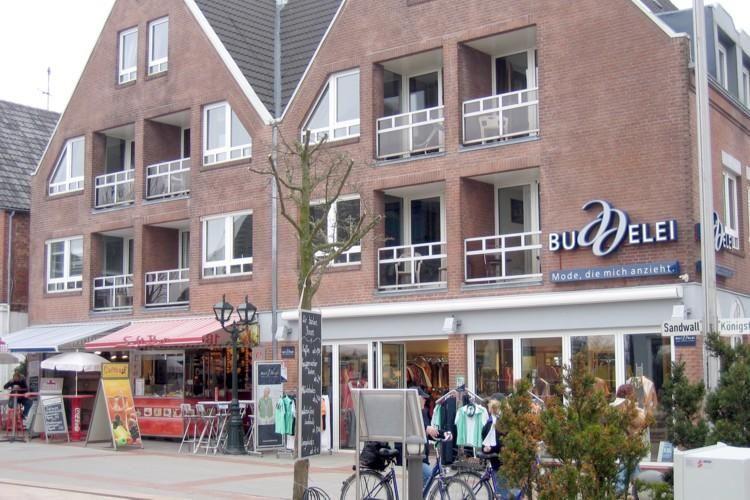 Fassade eines mehrstöckigen Gebäudes mit Balkonen und Geschäften im Erdgeschoss.