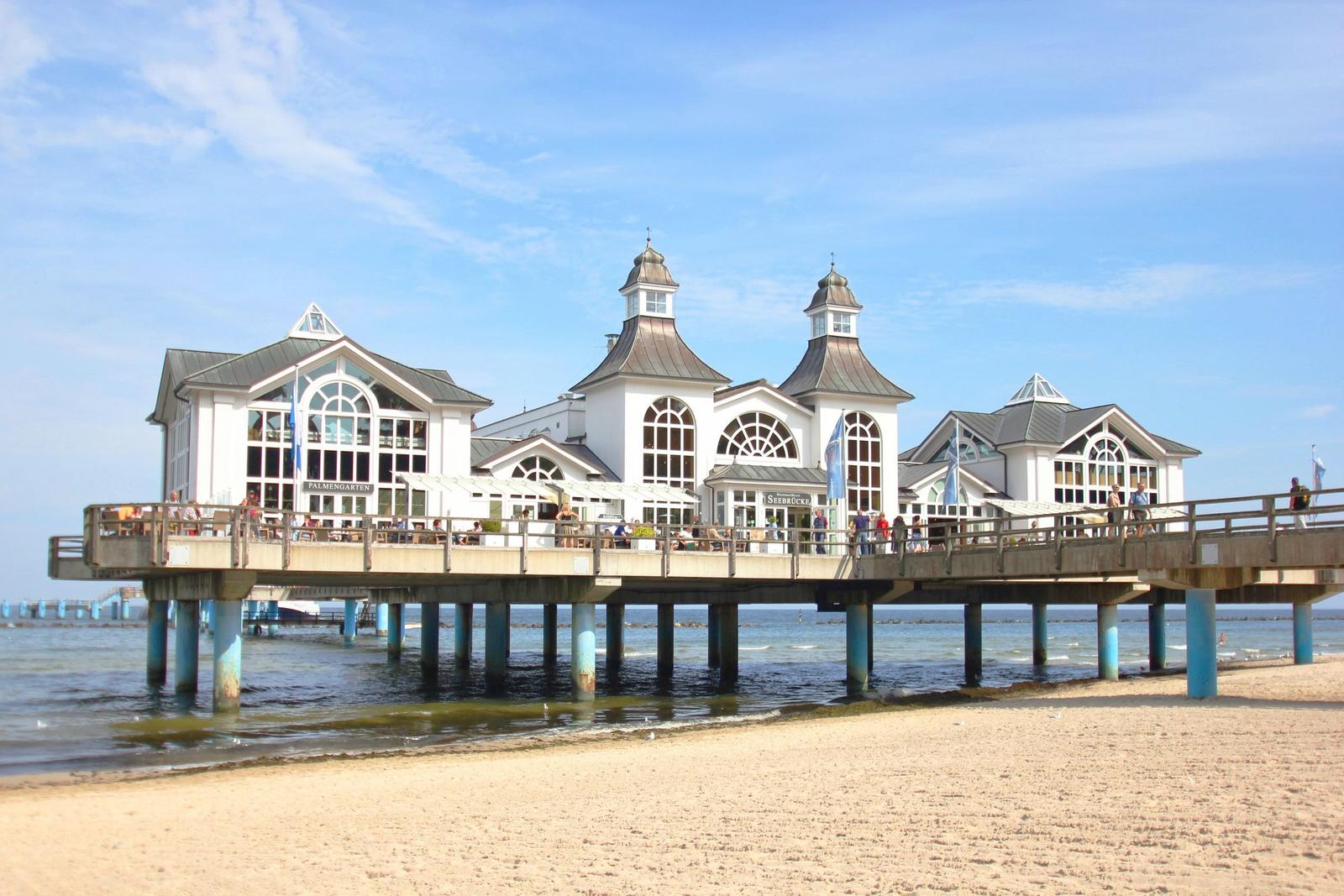 Hochgelegene Strandpromenade mit weißem Gebäude und Menschen. Blick auf das Meer.