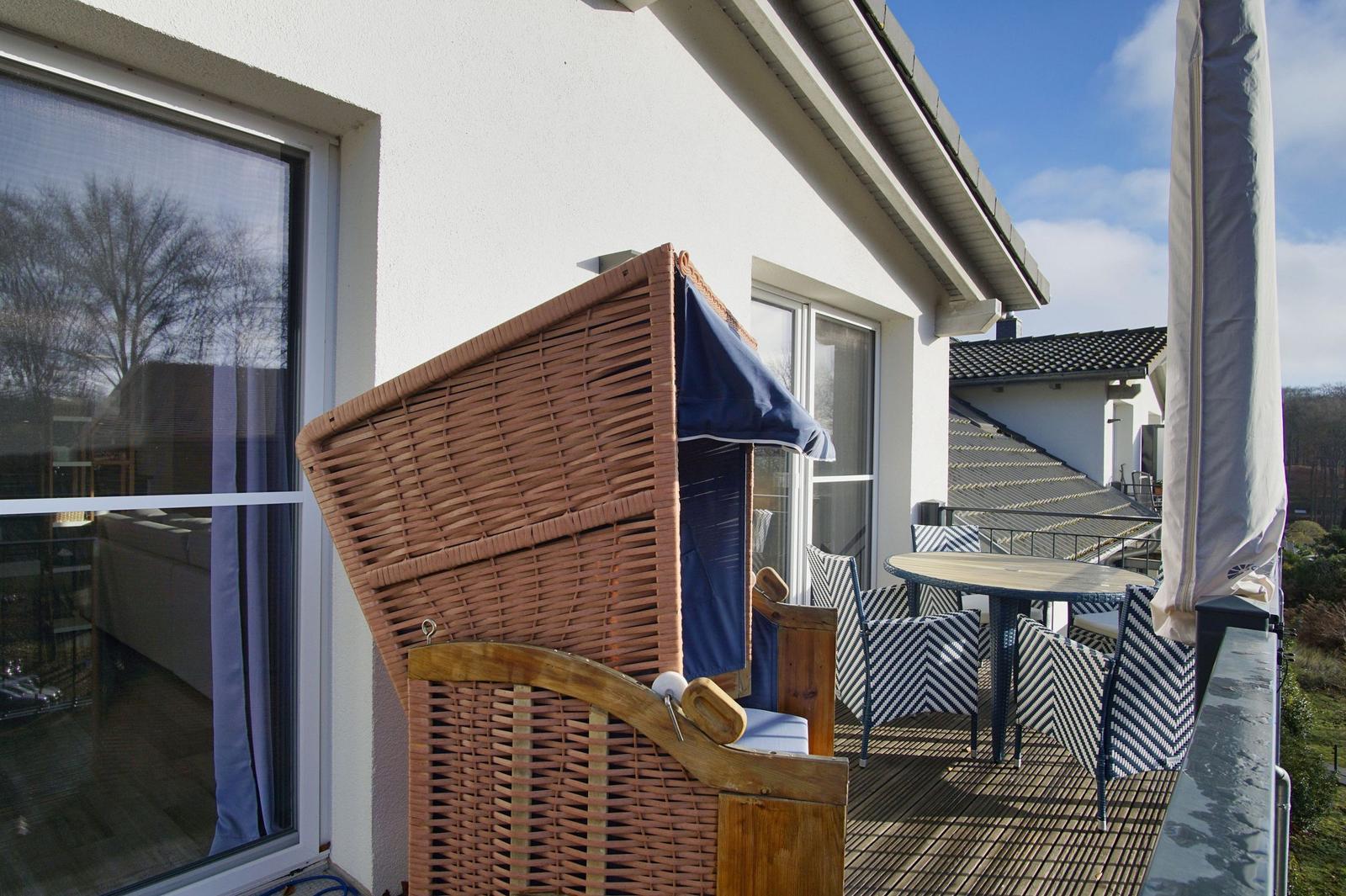 Terrasse mit Wickerliege, Tisch und Stühlen. Blick auf benachbarte Gebäude.