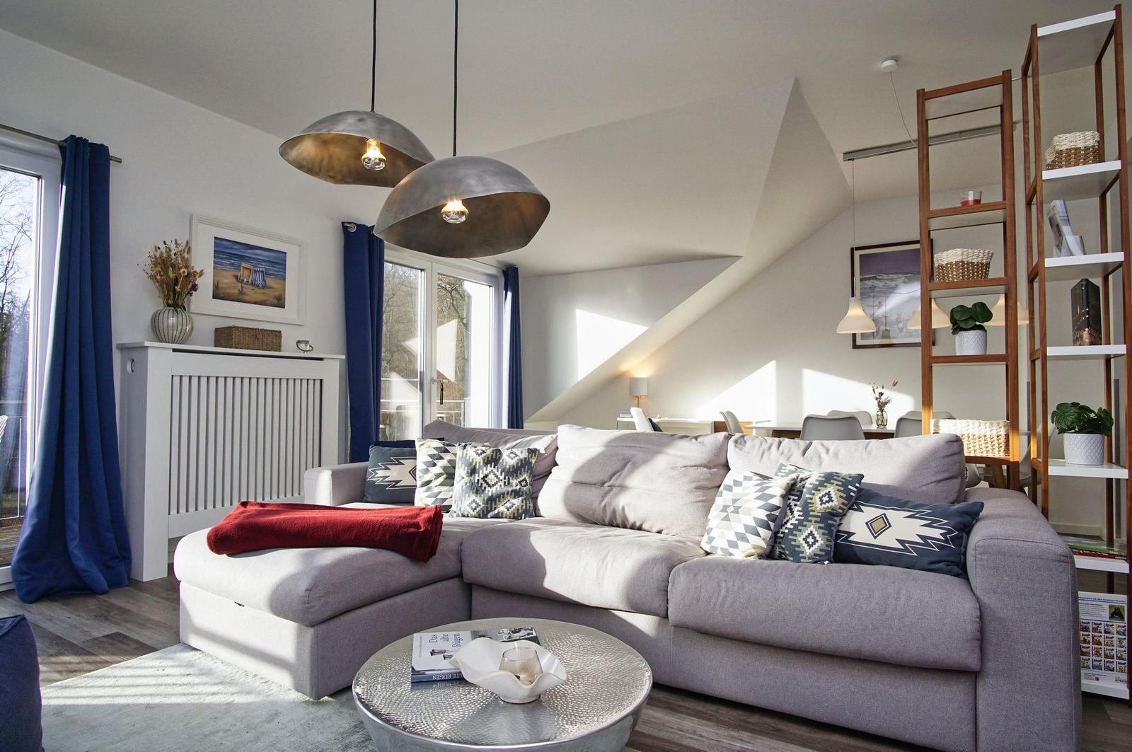 Wohnzimmer mit grauem Sofa, blauen Vorhängen und Holzboden. An der Wand hängt ein Bild.