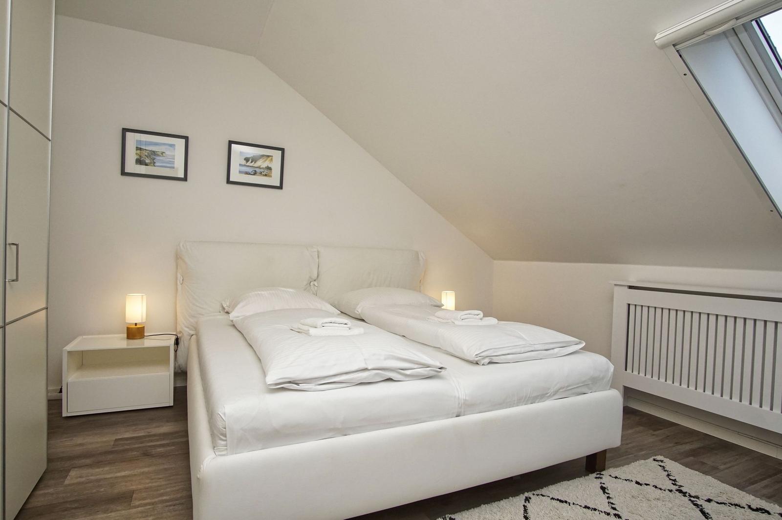 Schlafzimmer mit Doppelbett, Schrank, Nachttisch und Dachfenster.