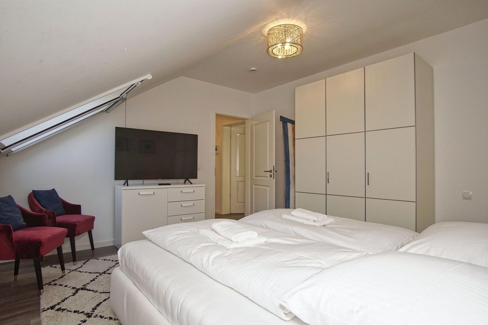 Schlafzimmer mit Doppelbett, Kleiderschrank, TV und roten Sesseln.